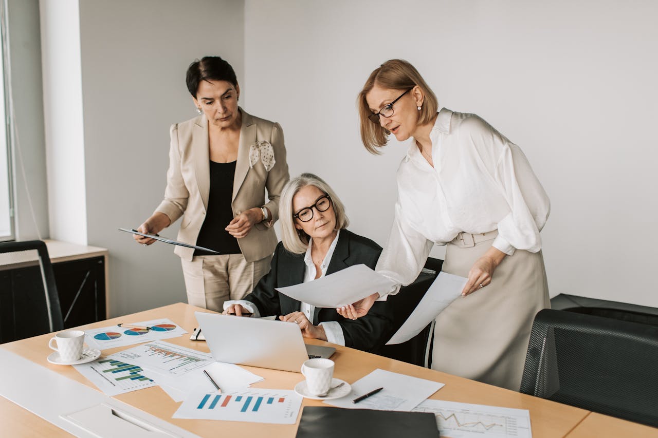 our-story Three businesswomen discussing reports in a modern office environment.