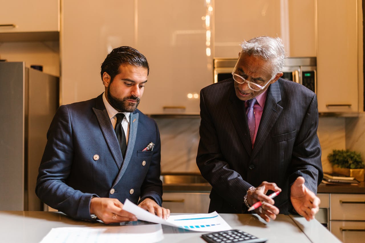 who-we-are Two businessmen engaged in a focused discussion over financial documents in a modern office setting.