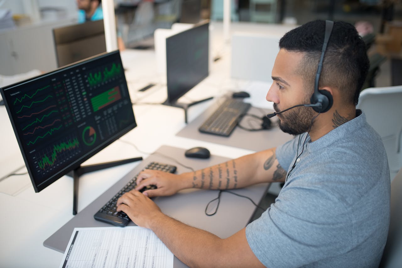 services-01 Man in a headset analyzing stock data on a computer monitor at his workspace.
