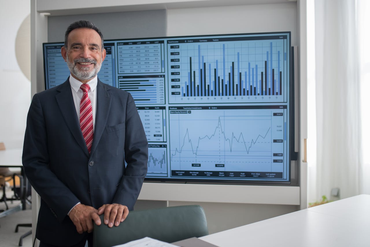 services-02 Smiling businessman in office analyzing financial graphs on a large screen, demonstrating professional success.