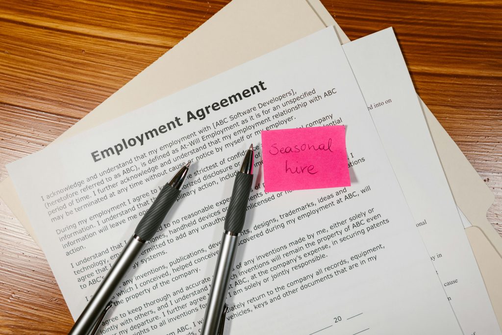 pexels photo 7841420 7841420 Top view of employment agreement contract with pens and seasonal hire note on wooden desk.